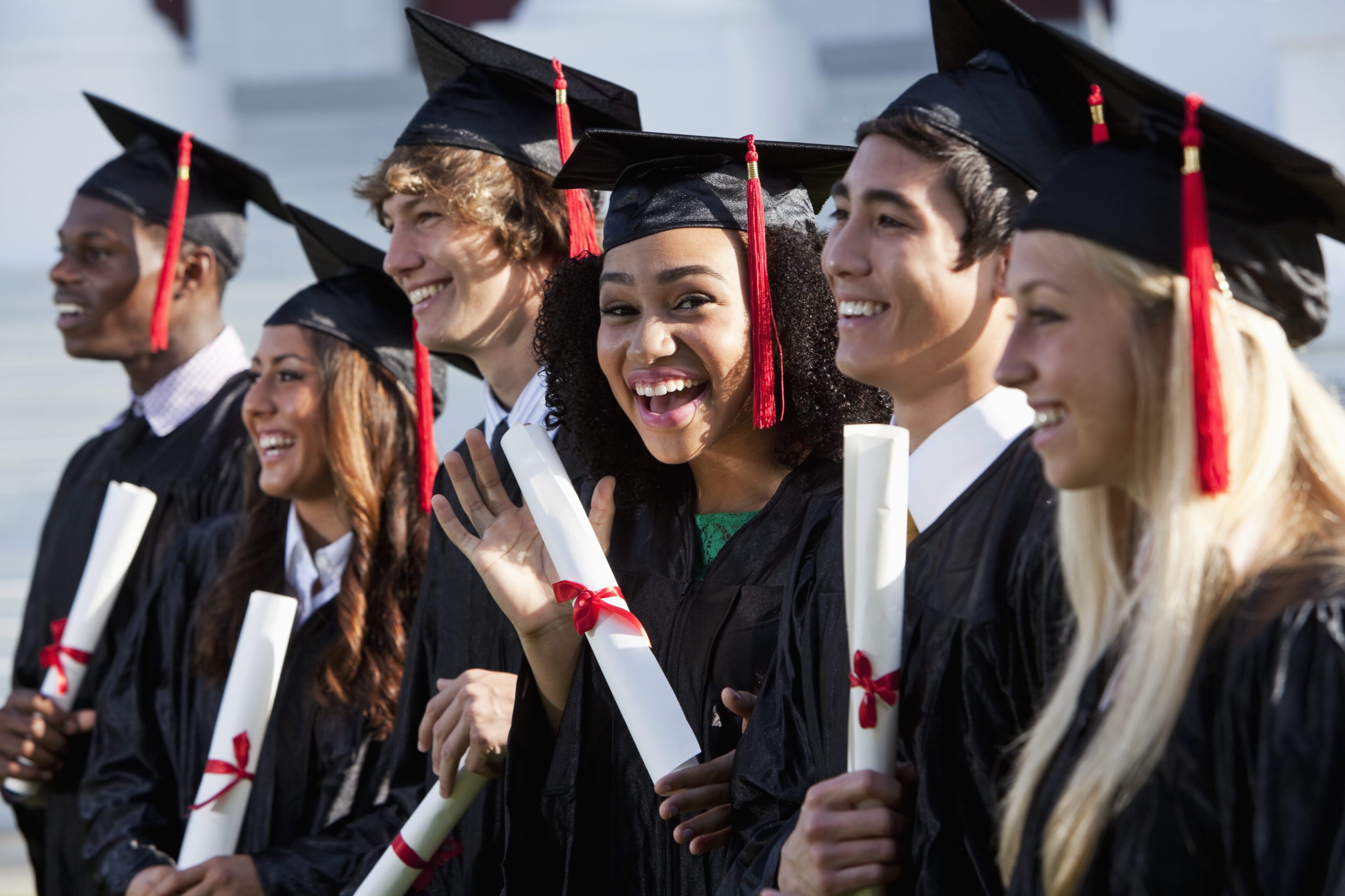 Graduating class Multi-ethnic friends graduating together, in cap and gown. Main focus on African American girl in middle, waving at camera.